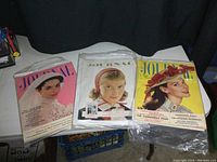 Three vintage Ladies' Home Journal magazines stacked side by side, showing different cover art featuring women in 1950s fashion.