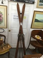 Front view of tall wooden skis leaning against a door with surrounding furniture and paintings.