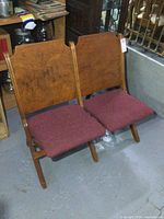 Pair of antique wooden stadium or theatre seats with wooden backs and dark red fabric seat cushions.