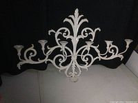Full view of vintage painted metal wall candle holder with six candle holders and scrollwork design against black background.
