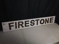Full view of white melamine board with five dark cast iron letters spelling 'FIRESTONE'.