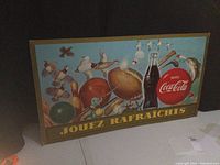 Front view of the vintage cardboard Coca-Cola sign with sports and outdoor game illustrations, French text, and minor edge wear.