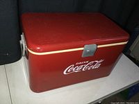 Top/front corner showing red lid with minor scratches, cream stripe around cooler, and logo.