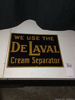 Full front view of rectangular DeLaval metal sign on white surface against dark curtain.