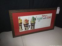 Framed vintage Coca-Cola paper sign with three floats, red matte, brown wood frame