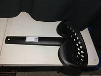 Full view of black metal Massey-Harris tractor seat with mounting arm lying flat on a table.
