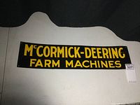 Full view of vintage McCormick-Deering Farm Machines embossed metal sign showing yellow lettering on black background, with curved decorative top edges.