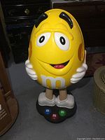 Front view of yellow M&M's resin candy store display showing facial detail and base with colored M&M buttons.