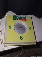 Front view of yellow square Mountain Dew clock with green numbers 3, 6, 9 and logo in upper left.