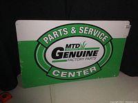Full view of the painted metal sign showing the MTD Genuine Factory Parts branding and text 'Parts & Service Center' in green and white on a white background with green oval logo.