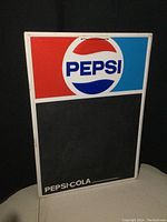 Full view of vintage metal embossed Pepsi chalkboard sign with Pepsi logo on top and blank chalkboard below.