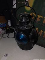 Front and side view showing black metal lantern with a large blue lens on one side and a large red lens on the adjacent side. Metal handle attached at the top.