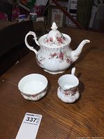 Image showing teapot, creamer, and sugar bowl with floral patterns and gold accents on wooden table.