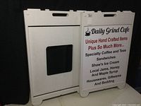 Two white folding resin sandwich board signs side by side, one showing the side with a black rectangular cutout, the other flat side with signage visible.