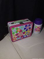 Front view of the metal lunchpail and the thermos beside it showing floral designs