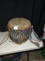 Full side view of the vintage drum showing the black and white patterned fabric, leather straps, and neck band.
