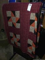 Full view of the quilt hanging, showing patchwork and checked border with warm color palette.