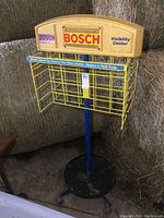 Frontal view of yellow metal wireframe double-sided Bosch display rack showing wire baskets, blue pole and black base on wheels.
