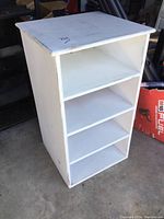 Front view of the white painted wooden cabinet showing three open shelves and the lift lid top.