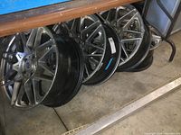 Overview of six silver-faced multi-spoke alloy wheels stacked under a table