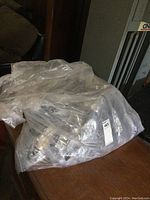Large plastic bag filled with multiple transparent sealed packages of disposable safety goggles.