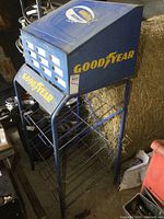 Full view of the blue metal hose rack with cabinet on top displaying yellow Goodyear logos.