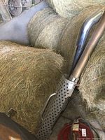 Photo showing stainless steel exhaust pipe with perforated heat shield and grab handle leaning against hay bales.
