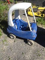 Front-side view of the blue Little Tikes kids push car with white roof showing outdoor wear and opening door hardware.
