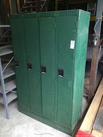 Front view of four-section green metal locker cabinet with visible lockable handles and ventilation slots.