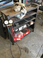 Metal shelf with four shelves showing surface rust, some wear, pressure gauges and attached hoses on side, measuring approximately 34x12x34 inches.