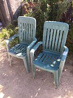 Pair of green resin deck chairs placed outside on a concrete surface with plants in background.