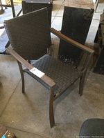 Angled side view of one plastic wicker patio chair with metal frame and wooden armrests, showing condition and material details.