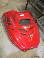 Red Ski-Doo hood shell for Rotax 500 Formula SL snowmobile shown from front angle with visible vents and mounting points, placed indoors on concrete floor.