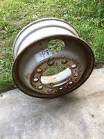 Front and side view of a white steel 22.5-inch heavy truck wheel rim showing circular stud piloted bolt holes with rust around them and on the surface.