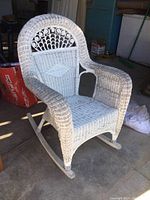 White wicker rocking chair, front angle showing arched back with decorative wicker work, thick armrests, and rockers.