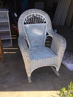 Front view of white wicker rocking chair showing woven seat, arms, and decorative rounded back with looped design.