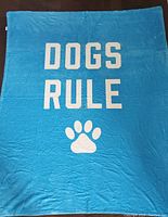 Blue plush throw blanket laid flat, showing the full text 'DOGS RULE' and paw print graphic.