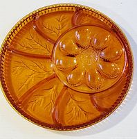 Full view of amber glass round plate with six egg-shaped sections and leaf pattern divisions, detailed beaded edge.