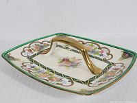 Angled view of rectangular porcelain candy dish with floral pattern and gold-tone handle