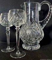 Photo showing the large cut crystal footed pitcher with detailed starburst and diamond cut patterns alongside two matching cut crystal footed goblets.