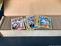 Box filled with multiple 1987 Topps baseball cards showing various players with gold-bordered card design, partially spread in box.