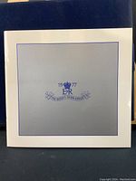 White folder with silver-blue embossed text and design "1977 E II R The Queen's Silver Jubilee"