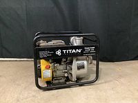 Front-left angled view of the Titan trash pump in black tubular steel frame showing yellow engine and printed specifications.