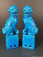 Front view of pair of blue glazed ceramic foo dogs on rectangular bases against black background.