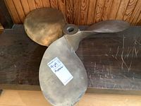 Three-blade brass propeller on wooden surface with label