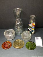 Photo of the entire lot showing all glass items: clear milk jar, small glass container with lid, dome lid trinket dish, crescent ridge milk bottle with marbles, and three colorful glass suncatchers