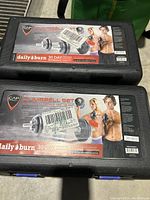 Two black plastic carrying cases labeled CAP 40 lb adjustable dumbbell set with images of people exercising and product info.