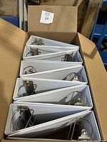 Open cardboard box containing six new white 4 inch binders with metal D-rings inside.