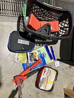 Full view of all items in black basket showing ice scraper, cleaning supplies pouches, packets and red handled item