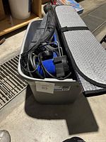 Full view of lot inside grey plastic bin showing assorted car accessories including cords and sunshade covers.